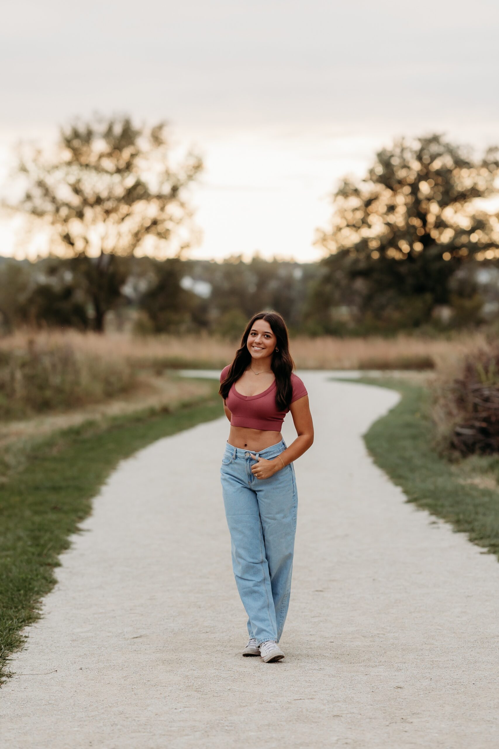 A happy plainfield north high school senior walks in a sand park path in a pink top and jeans